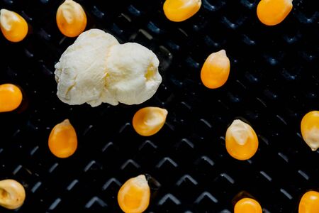 popcorn grains popped and not popped in top view, and closeup and black textured backgroundの写真素材