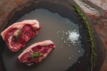 fresh raw beef loin, with salt and a sprig of rosemary on wooden backgroundの写真素材