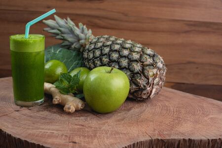 glass of juice and fresh ingredients for preparing detox green juice, kale leaf, ginger, lemon, mint, pineapple and green apple on wooden texture and with space for writingの写真素材