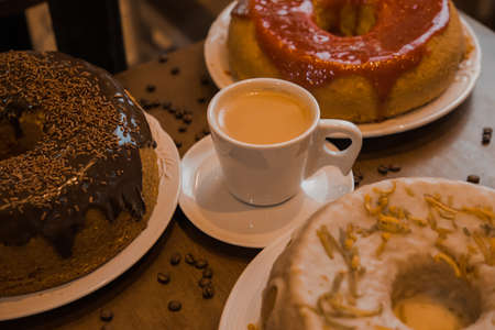 white cup of coffee with milk, with three cakes around it, on a wooden tableの写真素材