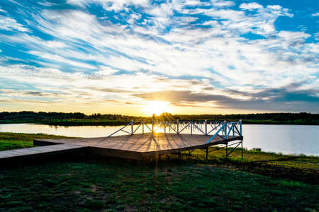Sunset on the summer pier by the lake with cloudsの写真素材