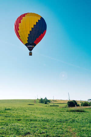 Multicolored hot air balloon on blue sky over village field verticalの写真素材