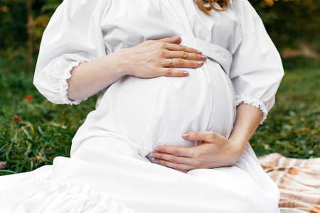 Close-up of a pregnant girl in a white dress in natureの写真素材