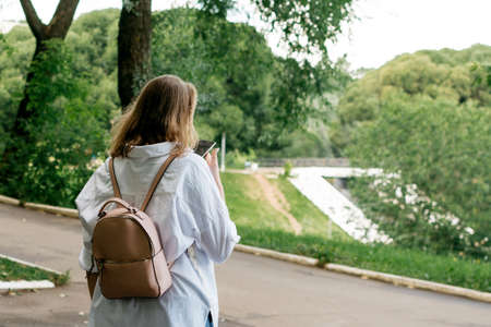 Girl in a white shirt with a phone from behind in a summer parkの写真素材