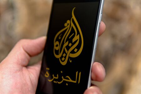 Tallinn/Estonia - September 18, 2019: Black phone with logo of news media Al Jazeera on the screen. News media icon. Hand with phone. Can be used as illustrative for marketing or business conceptのeditorial素材