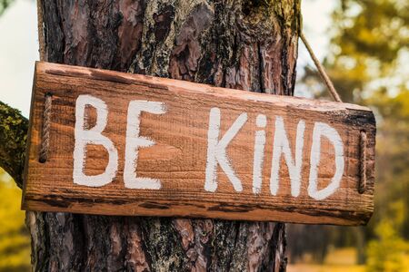 Wooden motivating sign on an old pine tree in the autumn park says "Be kind." Can be used as an illustration or marketing concept. Unity with natureの写真素材
