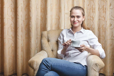 Beautiful young woman sitting with a cup of tea and drinkingの写真素材