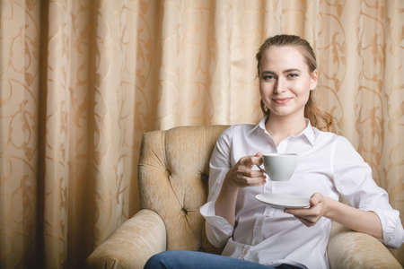 Beautiful young woman sitting with a cup of tea and drinkingの写真素材