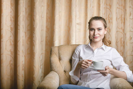 Beautiful young woman sitting with a cup of tea and drinkingの写真素材