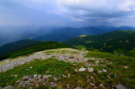 Mountain landscape with mossy green rocks and severe cloudy sky with rain in distance
