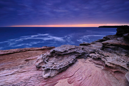 Sunrise seascape with orange rocks and ocean pools and sea shells with cloudy stormy sky and distant cliffsの写真素材