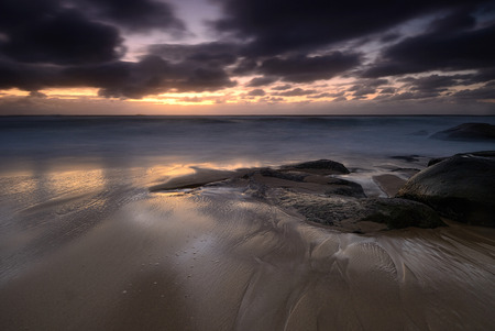 Moody sunrise seascape with colored clouds and flowing waterの写真素材