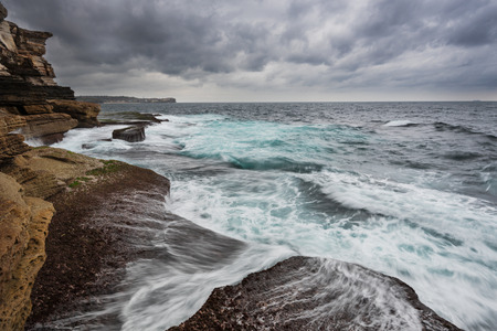 Stormy ocean in Sydney with gray heavy clouds and unsert sea with white foam and cyan colorの写真素材