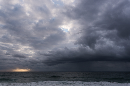 Approaching storm cloud with rain over the sea during sunriseの写真素材