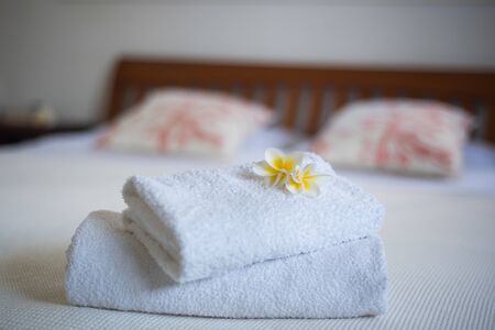 Frangipani flowers on the towels in the hotel room with bed in backgroundの写真素材