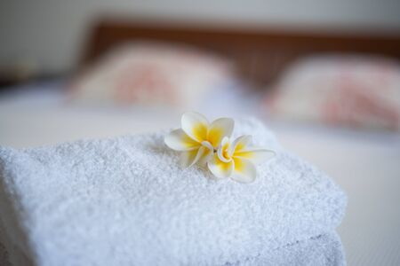 Frangipani flowers on the towels in the hotel room with bed in backgroundの写真素材