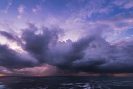 Approaching storm cloud with rain over the sea during sunriseの写真素材