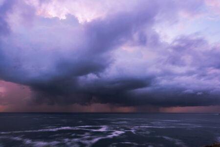 Approaching storm cloud with rain over the sea during sunriseの写真素材