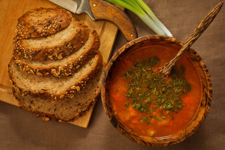 Rural-styled soup served in wooden utensils with wholegrain homemade bread an fresh green onion on the rude tableclothの写真素材