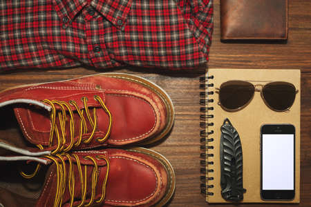 Worn but reliable boots, chekered vintage shirt, leather wallet, recycled paper notebook, cell phone, knife and sunglassesの写真素材