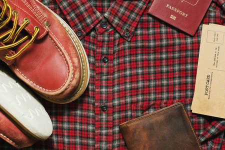 Old worn boots, leather wallet, vintage postcards and a passport on the checkered shirtの写真素材