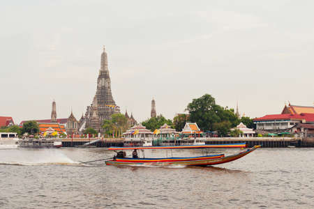 Cityscape with richly decorated biddhist temple and traditional thai longtail boatのeditorial素材