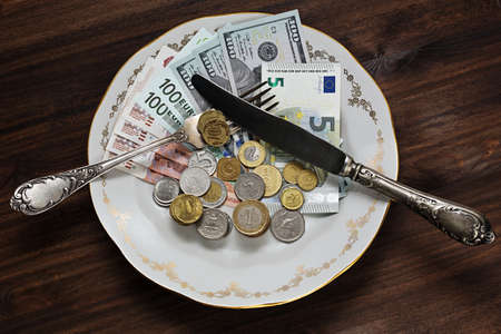 Bank notes and coins from different countries - US dollars, euros, russian rubles, turkish liras, czech krones, polish zlotys and so on on the plate with vintage utensils shooted like a mealの写真素材