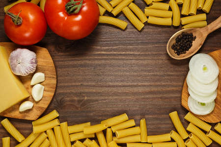 Pasta tortiglioni, tomatoes, onion, garlic, pepper and cheese are ready for cooking on wooden tableの写真素材