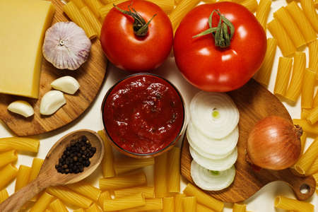 Different raw ingredients: dry pasta, tomatoes, tomato and basil sauce, onion, garlic, pepper and parmesan cheeseの写真素材
