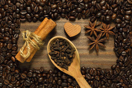 Cinnamon sticks, anise and clove in wooden spoon on the wooden table with frame of roasted coffee beansの写真素材
