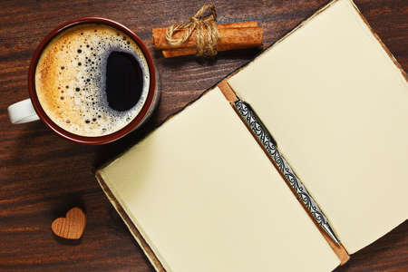 Cup with coffee stands on the wooden table near opened vintage diary and cinnamon sticksの写真素材