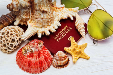 Russian passport covered by sea shells and starfish and sunglasses on the wooden deskの写真素材