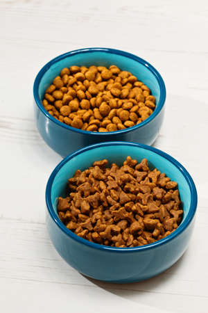 Two blue bowls full of cat's or dog's food standing on the floor - vertical shoot