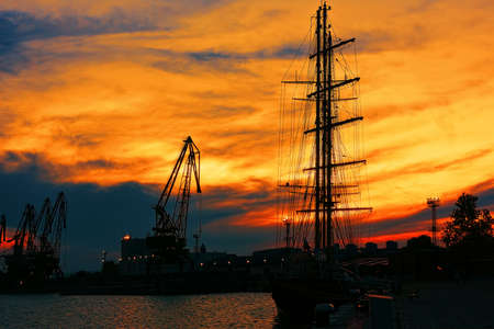 VARNA, BULGARIA - MAY 24, 2017: Sailboat and port cranes in Varna commercial harbor in sunsetのeditorial素材