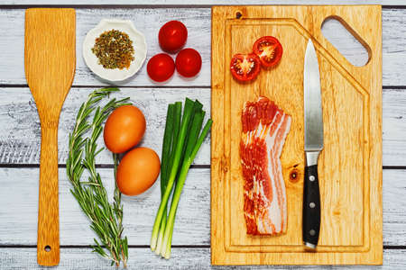 Raw cooking ingredients for omelette, scrambled or fried eggs cooking on the wooden table - eggs, pork bacon, cherry tomatoes, herbs and spices mixの写真素材