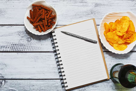 Keeping a diary or day planning concept with a bottle of beer and different snacks on rough wooden tableの写真素材