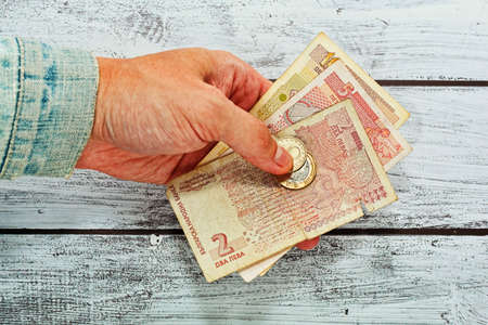 Man giving someone few bulgarian money. Paying debt concept. Worn old jeans jacket, old banknotes, rough skin.の写真素材