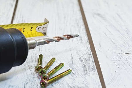 Heavy drilling machine, roll ruler and few screws on the wooden desk. Close-up capture with lens...
