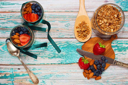 Preparing healthy breakfast for two persons - multigrain muesli served with almond, strawberry and blueberry in tiny glass jars on rural style wooden table. Top view.の写真素材