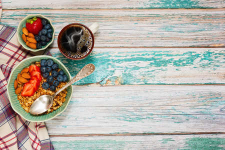 Healthy and nutritious in rural style - bowl with multigrain granola and fresh berries - strawberry and blueberry, cup with coffee. Served on rough painted table.の写真素材