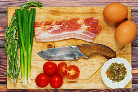 Ingredients prepared for cooking in flat lay - eggs, pork bacon, cherry tomatoes, onion, rosemary and dried herbs mix. Nutritious meal recipe. Top view.の写真素材