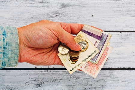 Male hand with rough skin in old and worn jeans jacket holding few old and used bulgarian currency paper - paying debt concept, poverty symbol.の写真素材