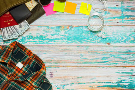 Preparing for outdoor activity concept - checkered shirt, bag with passport, money and smartphone, sticky notes with place for text and a glass of water on rough painted wooden table. Flat lay.の写真素材