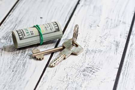 Stack of US currency paper - dollars - and a pair of door lock keys. Loan contribution or rental payment concept. Close-up capture with selective focus.の写真素材