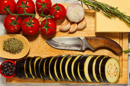 Different ingredients for grilled eggplant mediterranean dish cooking - sliced eggplant, cherry tomatoes on branch, cheese, garlic, rosemary and herbs and spices mix. Rural style recipe. Top view.の写真素材