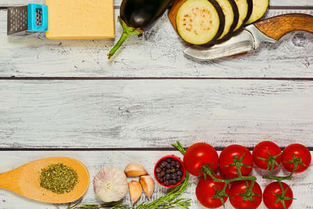 Mediterranean dish cooking idea - ingredients in flat lay capture. Sliced fresh eggplant, tiny sweet tomatoes, ripe cheese, organic garlic and rosemary, different herbs and spices mix. Place for text.の写真素材