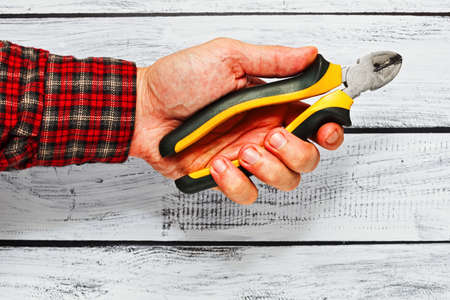 Male hand with cutters in it over wooden background. Person is wearing classic work checkered shirt...