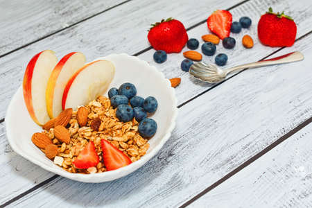 Ready to eat nutritious breakfast made of fresh organic ingredients - wholegrain granola, apple, blueberry, strawberry, almonds. Healthy dieting concept. Close-up capture, selective focus.の写真素材