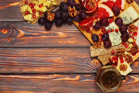 European way lunch with assortment of cheese served with grapes, grapefruit, pomegranate, walnut, crackers and jam. Good wine appetizer, healthy nutritious snack. Top view with place for text.の写真素材