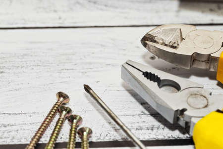 Close-up capture of some hand tools of worker, builder or repairman - pliers, nippers, screwdriver and screws on rough wooden background. Selective focus.の写真素材